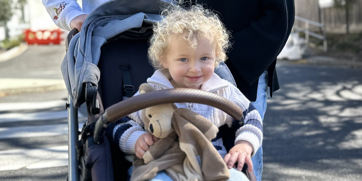Mitchell is sitting in a pram and smiling while holding a soft toy