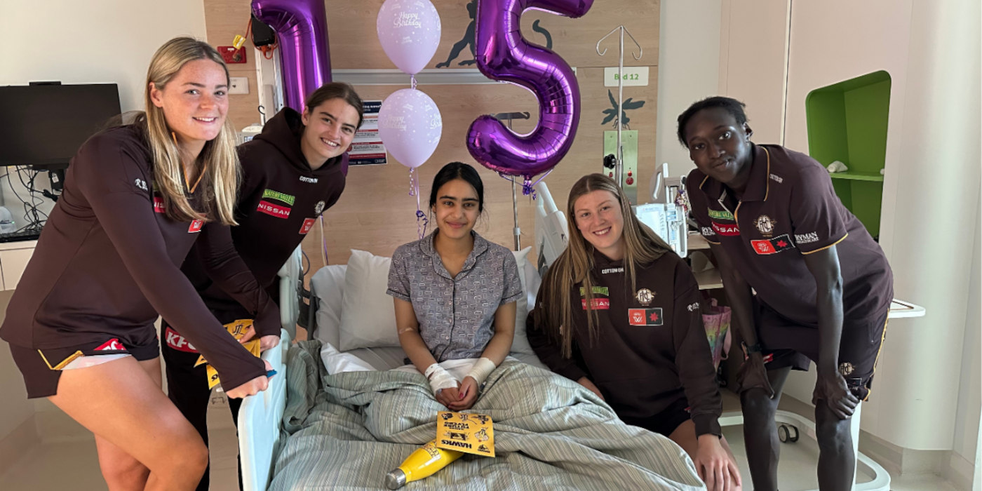 Hawks AFLW players take a photo with a girl in a hospital bed, with ballons behind her that read happy birthday and 15