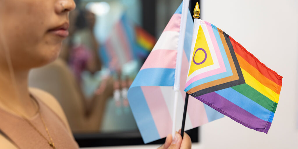 A woman holding a small transgender flag and an LGBTIQA+ flag