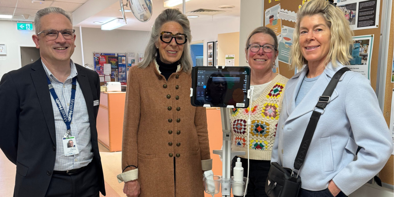 Four people smiling in a clinical setting with a medical device