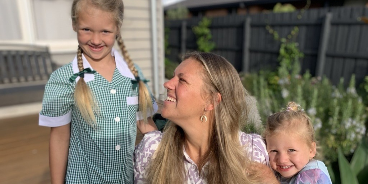 A woman smiles as they are embraced by two children in an outdoor setting.