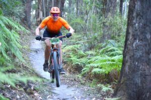 Alex riding a mountain bike fast downhill on a rainforest trail.