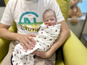 A person holding a baby wrapped in a blanket with a teddy bear pattern.