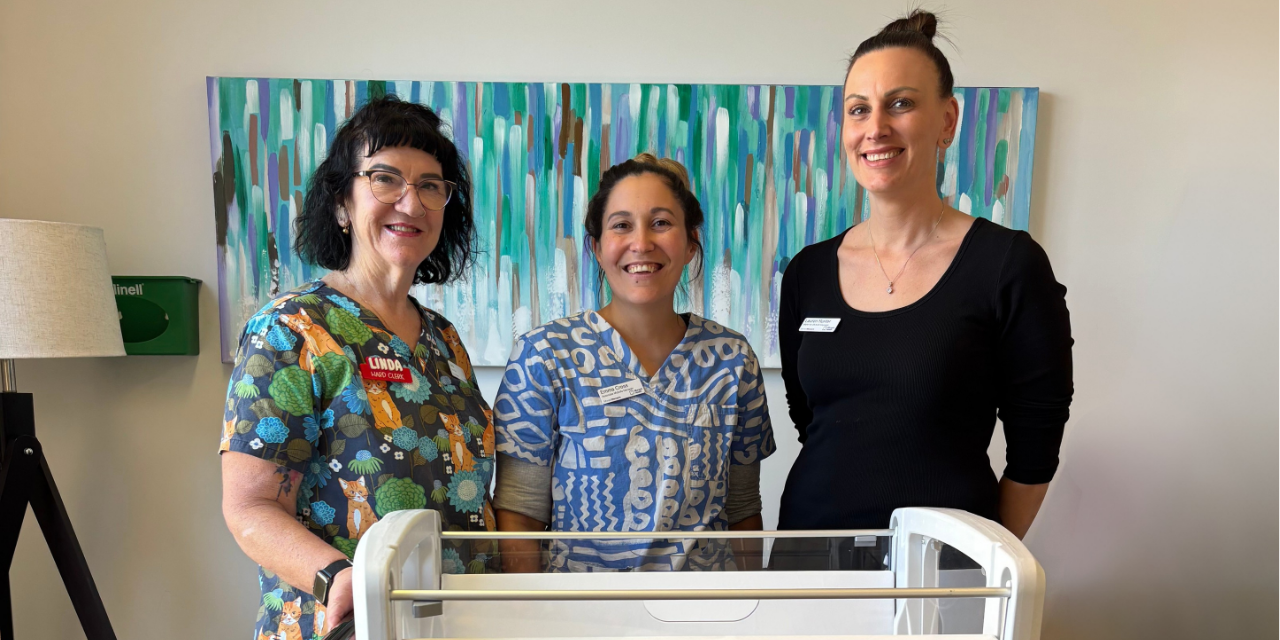 3 employees pose behind a new hospital cot