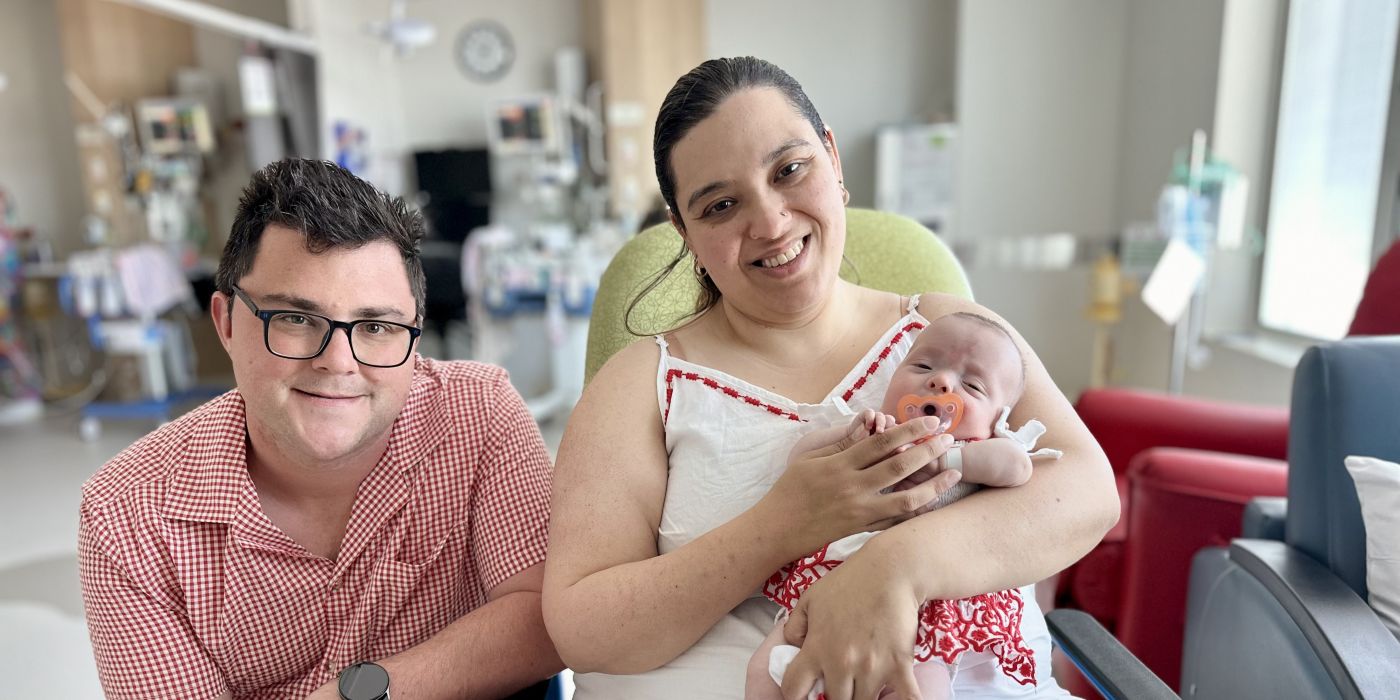 A man next to a woman sitting in a chair, holding a newborn