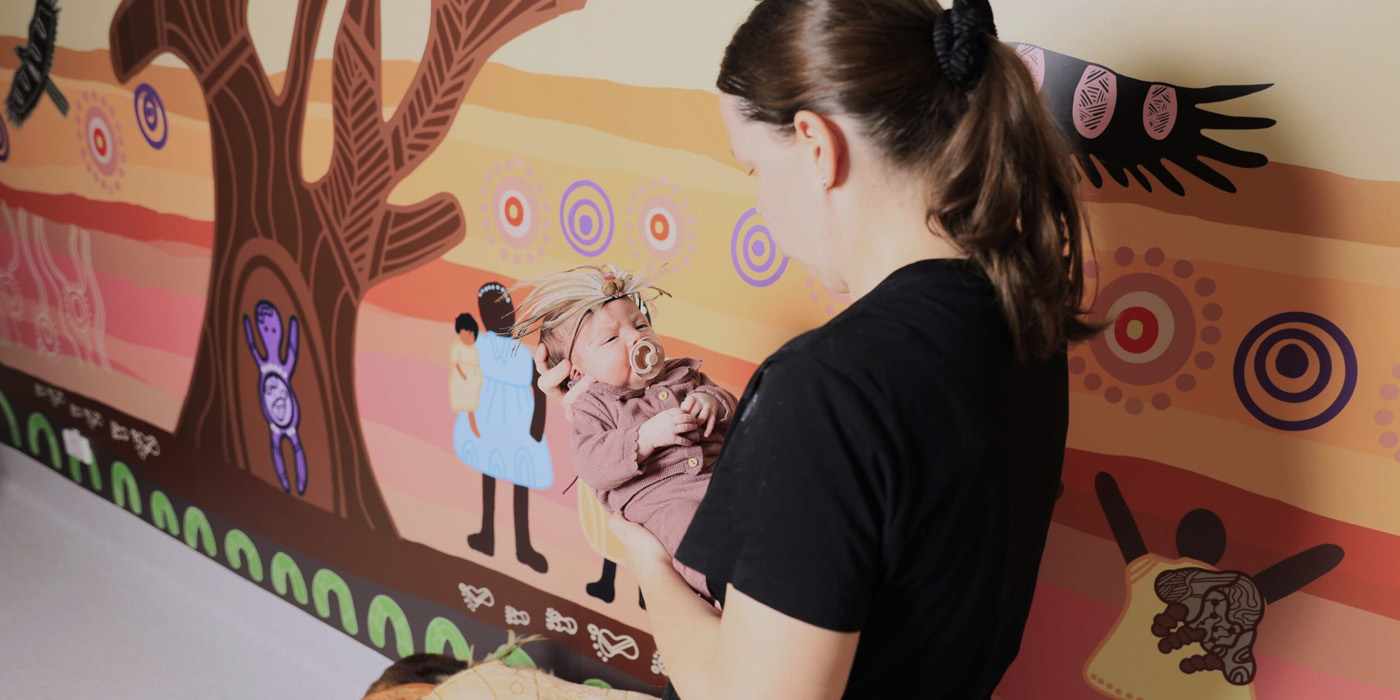A newborn is held in front of the Bubup Dreaming artwork