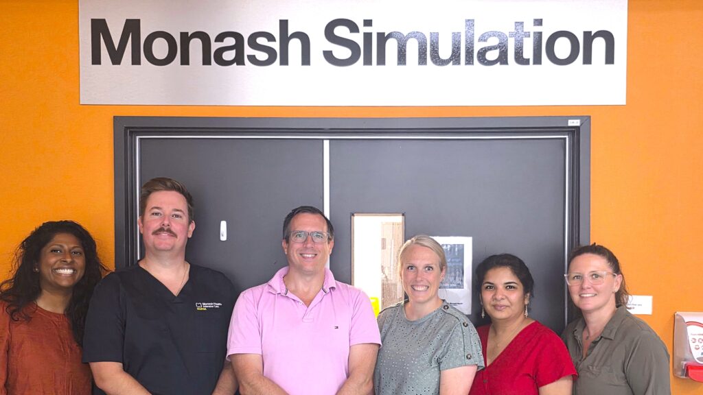 Group standing in front of Monash Simulation sign on orange wall