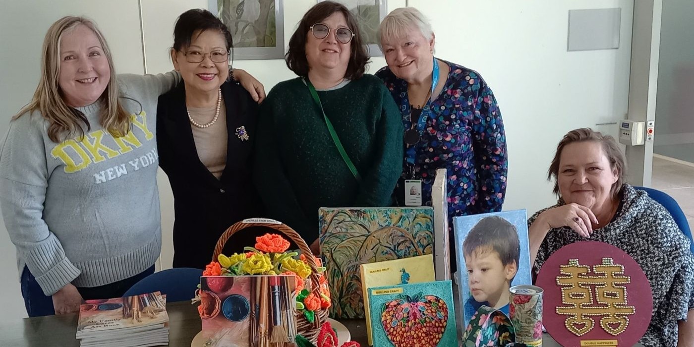 A group of people stand behind a desk with an assortment of artworks and copies of 'My Family Carer Art Book'