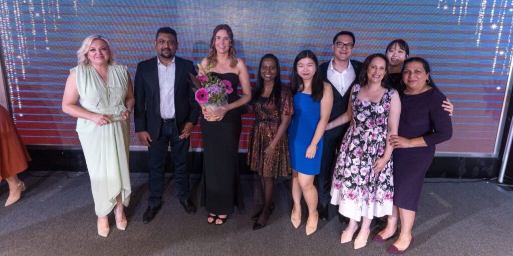 A group of smiling people in smart evening wear pose for a photo with an award.