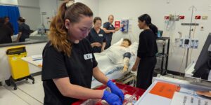 Medical staff preparing supplies near a hospital bed with a patient and other staff in discussion.