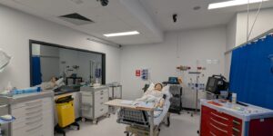Hospital room with medical equipment and a patient mannequin on a bed.