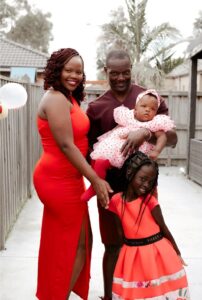 Four people posing for a family portrait with a dad holding a baby and a mum standing next to their daughter