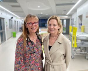 Two women standing together and smiling with a hospital ward in the background