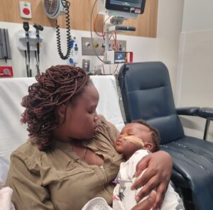 A woman is holding her baby while sitting on a patient bed