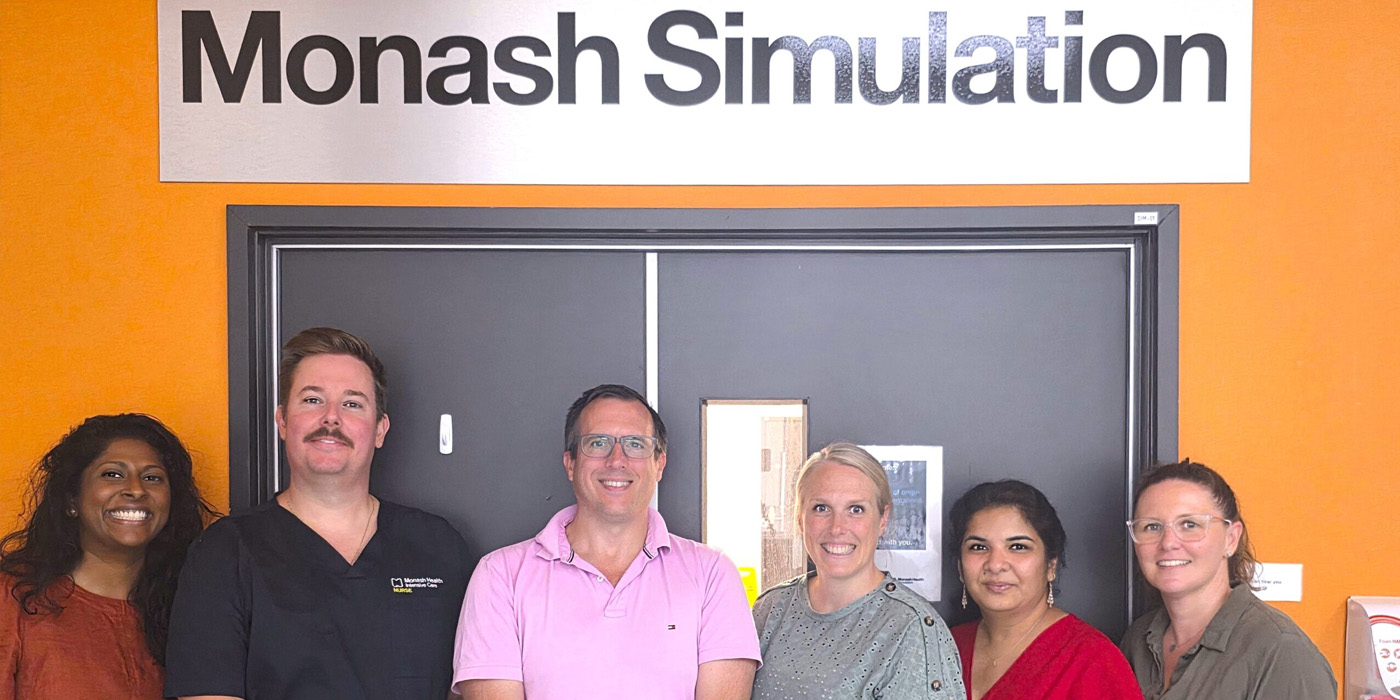 Group standing in front of Monash Simulation sign on orange wall