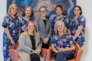 Seven people, most dressed in colourful scrubs, stand and sit together, smiling