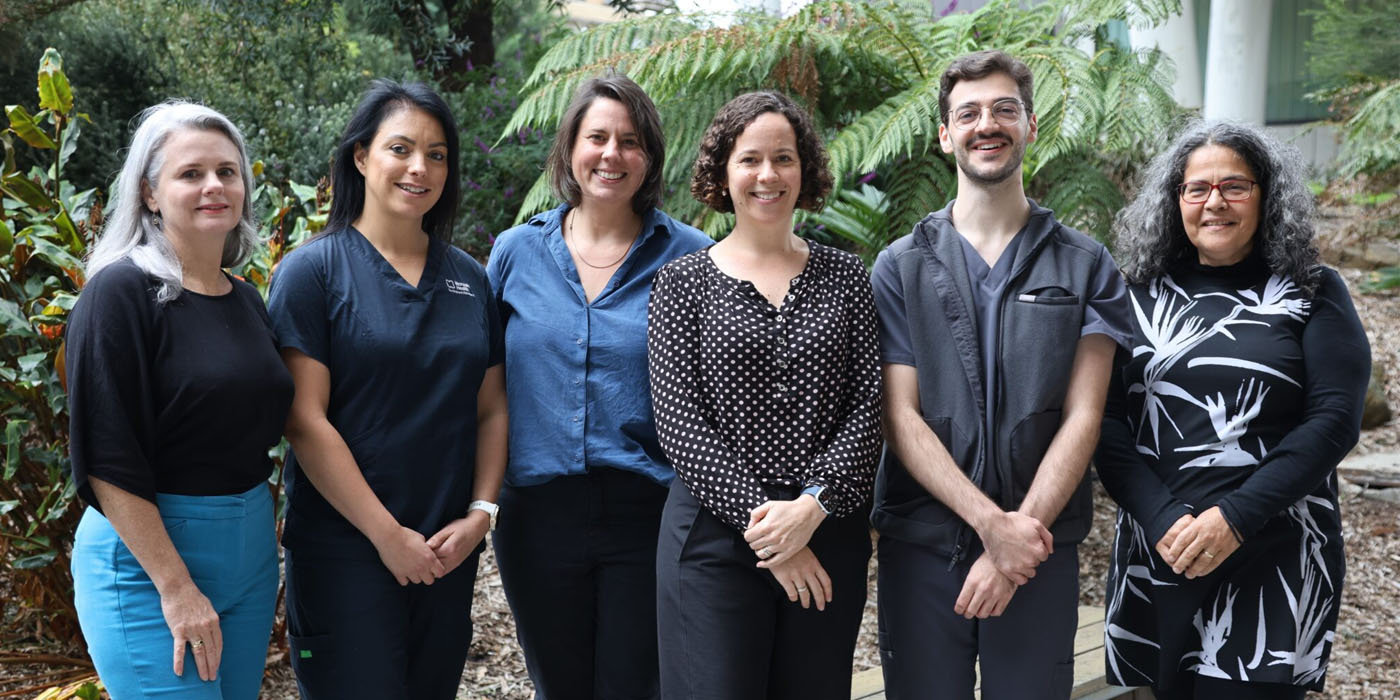 A group of 6 clinicians standing together and smiling in front of a garden