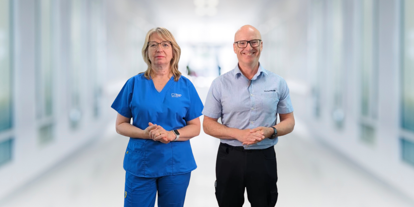 Two smiling health workers standing in a bright white hospital corridor.