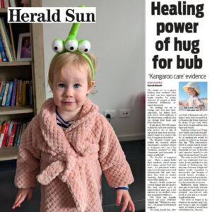A photo of a 2-year-old girl wearing a pink dressing gown and green character headband. Alongside the photo is a newspaper clipping, titled: Healing power of hug for bub.