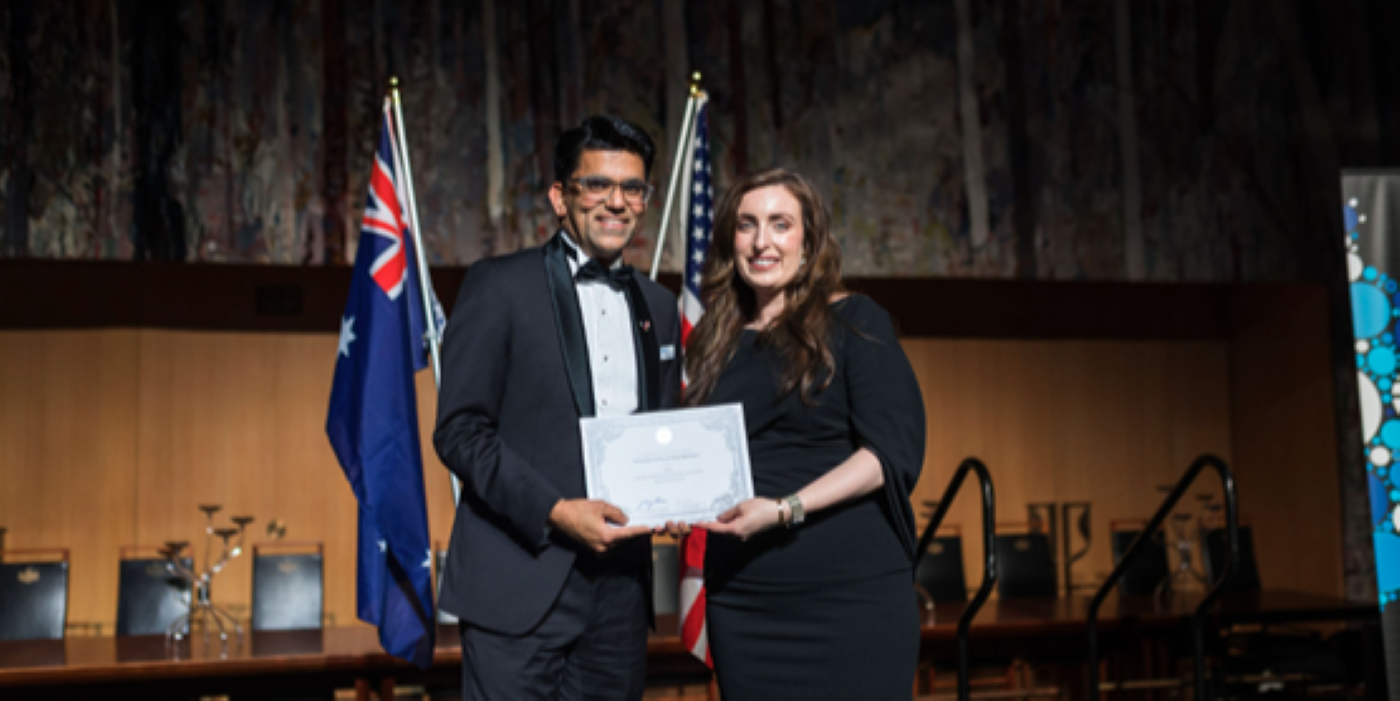 Associate Professor Atul Malhotra accepting a certificate, in front of Australian and American flags.