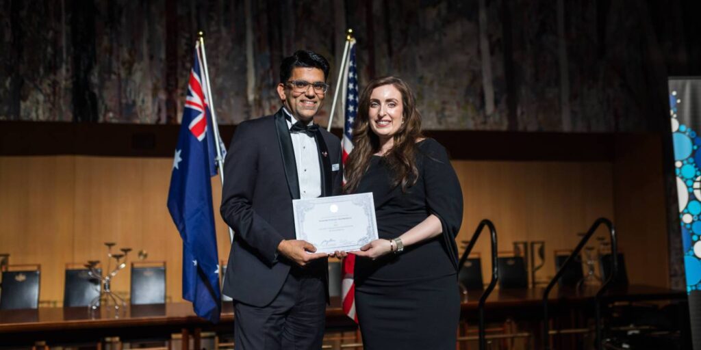 Associate Professor Atul Malhotra accepting a certificate, in front of Australian and American flags.