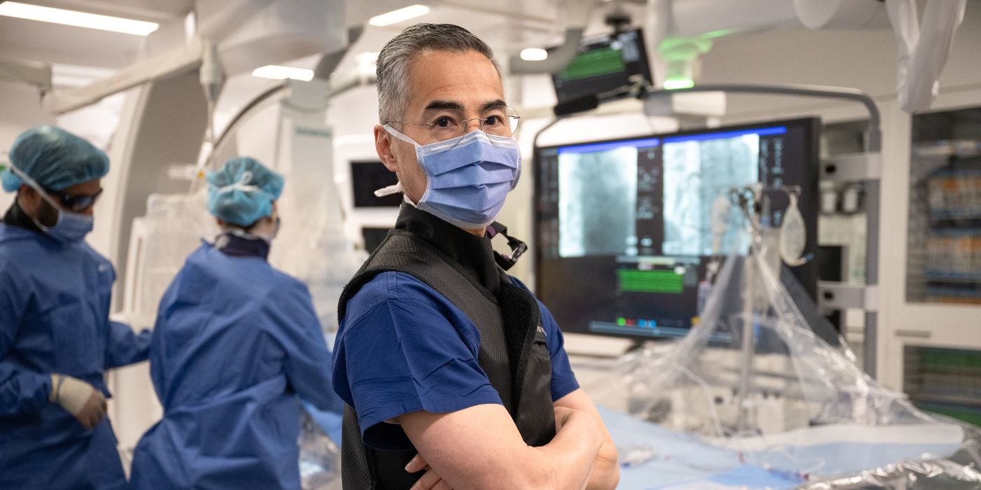 Professor Derek Chew in surgical attire working in a modern operating room with advanced imaging equipment.