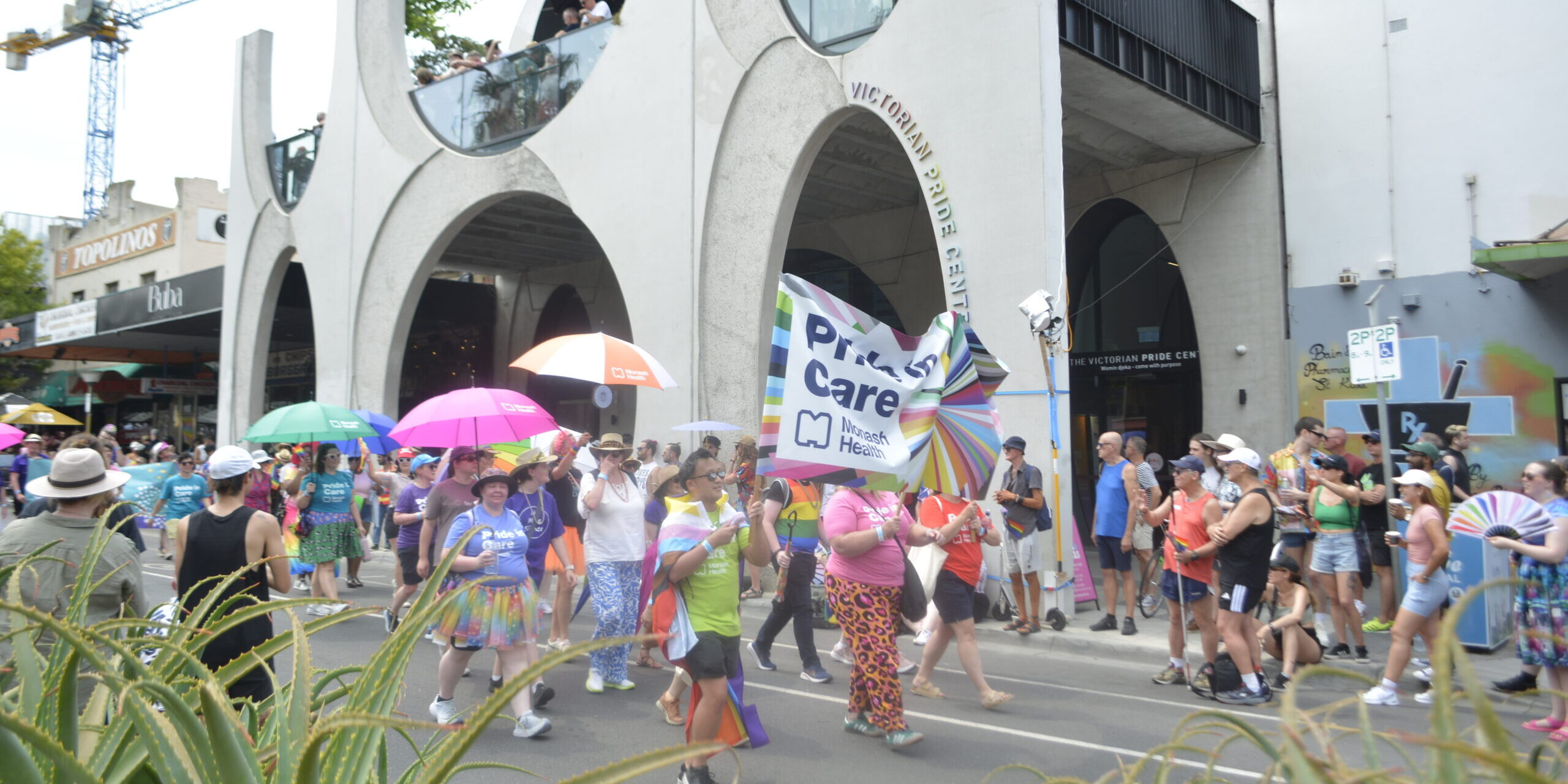 Photo of Monash Health employees marching in colourful clothes and a large banner in front of the Victorian Pride Centre