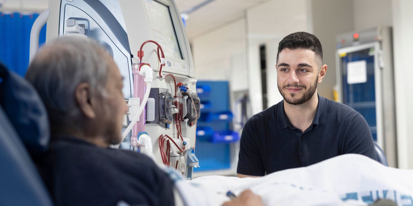 An employee at a health service sitting listening to a male patient who is undergoing dialysis. Monash Health will trial an AI language translation tool to support patients who speak a language other than English.