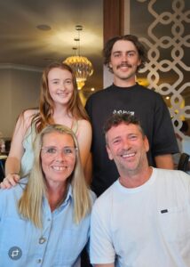 Two adults seated and two teenagers standing behind them, posing together in a restaurant.