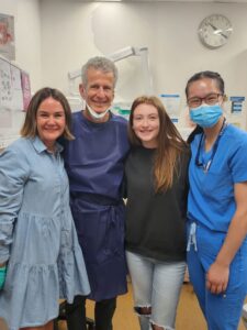 Smiling clinicians and a patient posing for a photo in a dental consulting room.